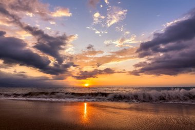 Kum kıyısına bir dalga gibi çarpan Güzel Renkli Okyanus Günbatımı