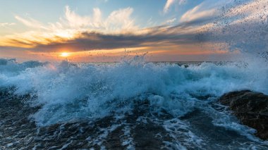 Sahilde yüksek çözünürlüklü görüntü formatında bir gündoğumu okyanus dalgası kırılıyor.