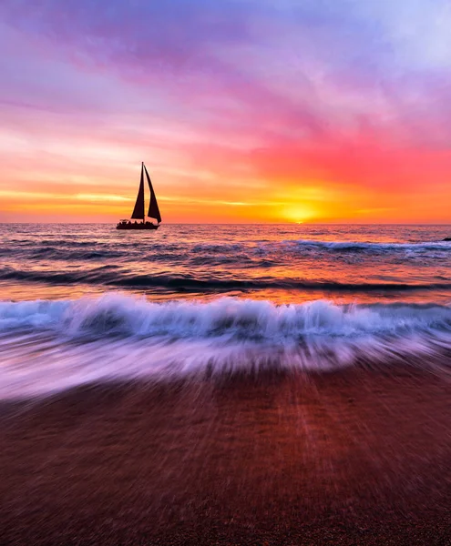 A Sailboat Is Sailing Along The Ocean With A Wave Breaking On Shore In Vertical Image Format