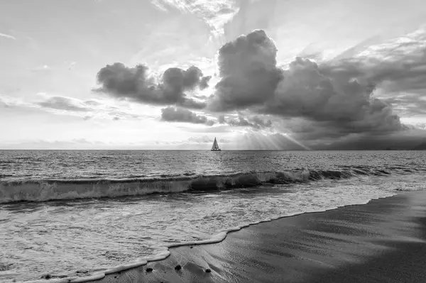 A Sailboat Is Sailing Along The Ocean With Sun Rays Breaking Through The Clouds Black And White