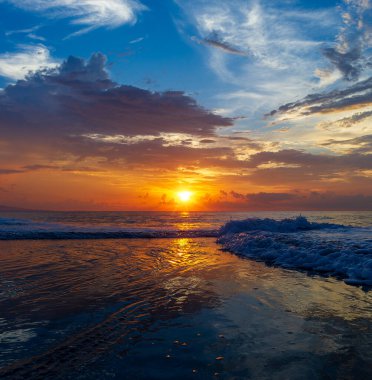 Okyanustaki güneş batarken kıyıda bir dalga kırılıyor.