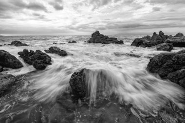 Geniş açılı deniz taşları manzaralı güzel bir okyanus batımı ve kara beyaz bir dalganın dalgalanması.