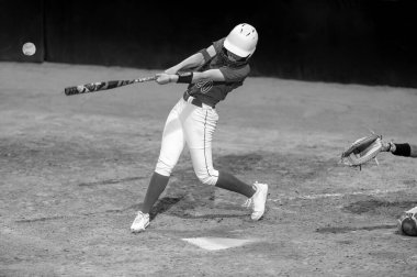 Bir softball oyuncusu beyzbol topuyla temas kurmak için yarasayı sallıyor.