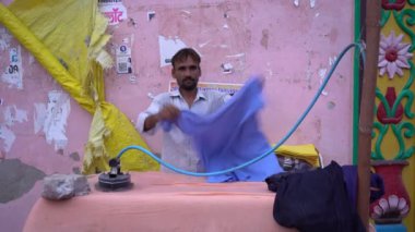 VRINDAVAN, INDIA Eylül 01, 2022: Vrindavan pazarının sokaklarında kıyafetlere ütü yapan adam.