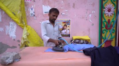 VRINDAVAN, INDIA Eylül 01, 2022: Vrindavan pazarının sokaklarında kıyafetlere ütü yapan adam.