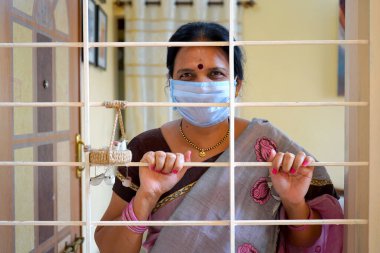 Karantinadaki kadın maske takıp pencereden bakıyor. Coronavirus / Covid-19 salgını.