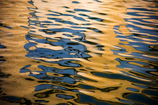 Water surface with moving wave of golden water reflecting sunlight
