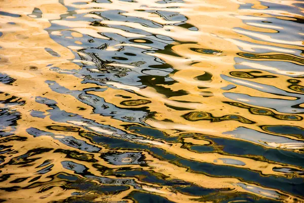 Water surface with moving wave of golden water reflecting sunlight
