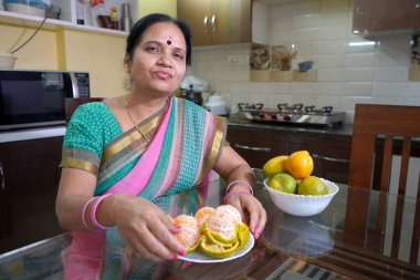 Kahvaltı masasında portakallı kadın, portakal yiyen Hintli kadın. Sağlıklı beslenme konsepti..