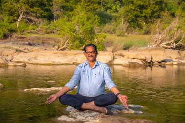 Nehirdeki bir kayanın üzerinde meditasyon yapan adam..