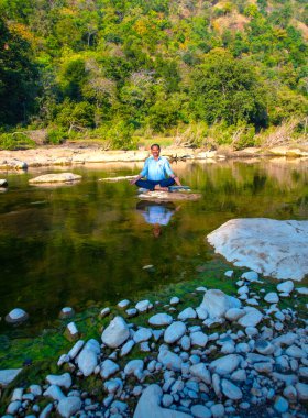 Nehirdeki bir kayanın üzerinde meditasyon yapan adam..