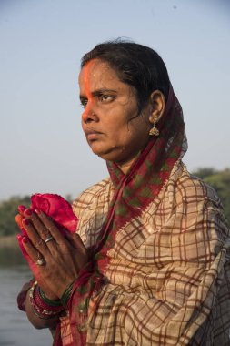 Traditionally dressed Indian woman pray into the river on Chhat Puja Festival. clipart