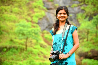 Güzel genç bir kadın ormanda kamerayla fotoğraf çekiyor. Gülümseyen kız havadan, rahatlıktan, yaşam tarzından hoşlanıyor..