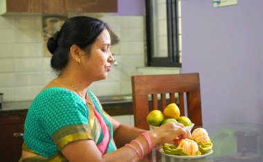 Kahvaltı masasında portakallı kadın, portakal yiyen Hintli kadın. Sağlıklı beslenme konsepti..