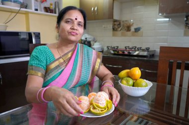 Kahvaltı masasında portakallı kadın, portakal yiyen Hintli kadın. Sağlıklı beslenme konsepti..