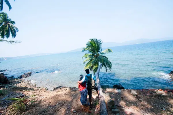 Denizin önünde oturan genç çiftin arka görüntüsü.