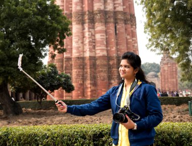 Qutub Minar, Delhi, Hindistan 'ın önünde selfie çubuğu ve akıllı telefonla selfie çeken güzel genç bir kadın..