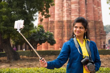 Qutub Minar, Delhi, Hindistan 'ın önünde selfie çubuğu ve akıllı telefonla selfie çeken güzel genç bir kadın..