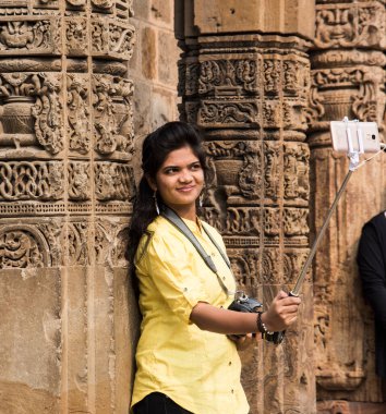Qutub Minar, Delhi, Hindistan 'ın önünde selfie çubuğu ve akıllı telefonla selfie çeken güzel genç bir kadın..