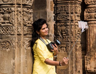 Qutub Minar, Delhi, Hindistan 'ın önünde selfie çubuğu ve akıllı telefonla selfie çeken güzel genç bir kadın..