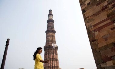 Qutub Minar, Delhi, Hindistan 'ın önünde selfie çubuğu ve akıllı telefonla selfie çeken güzel genç bir kadın..