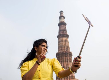 Qutub Minar, Delhi, Hindistan 'ın önünde selfie çubuğu ve akıllı telefonla selfie çeken güzel genç bir kadın..