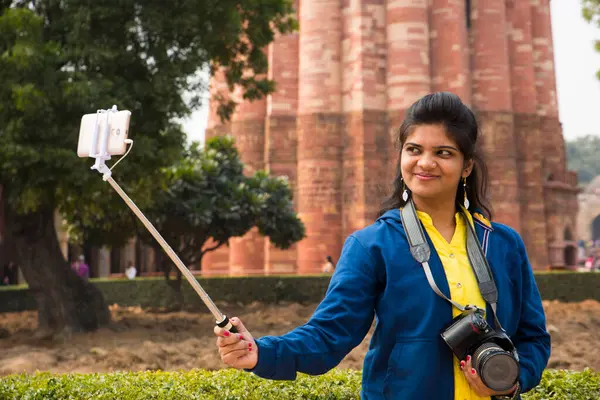 Qutub Minar, Delhi, Hindistan 'ın önünde selfie çubuğu ve akıllı telefonla selfie çeken güzel genç bir kadın..