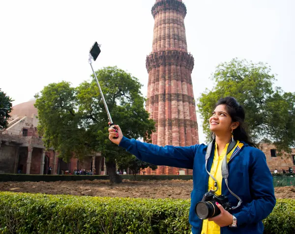 Qutub Minar, Delhi, Hindistan 'ın önünde selfie çubuğu ve akıllı telefonla selfie çeken güzel genç bir kadın..