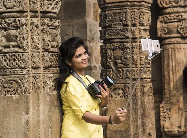 Qutub Minar, Delhi, Hindistan 'ın önünde selfie çubuğu ve akıllı telefonla selfie çeken güzel genç bir kadın..