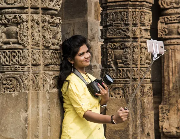 Qutub Minar, Delhi, Hindistan 'ın önünde selfie çubuğu ve akıllı telefonla selfie çeken güzel genç bir kadın..