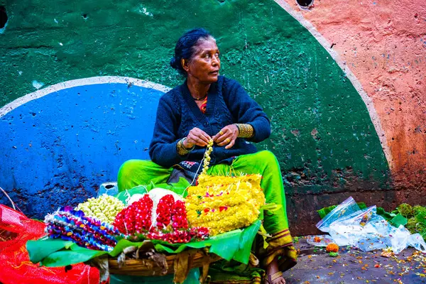 MUMBAI, INDIA, 28 ARALIK 2024: Dadar İstasyonu yakınlarındaki çiçek pazarında satmak için çiçek çelengi yapan kadın.