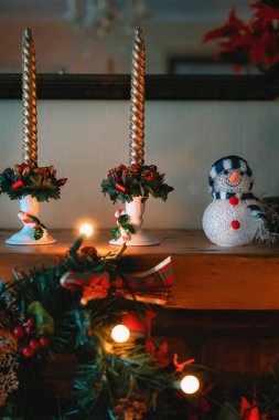 Festive Setting with Christmas Themed Candles, Snowman and Wreath on top of Fireplace with Fairylights clipart