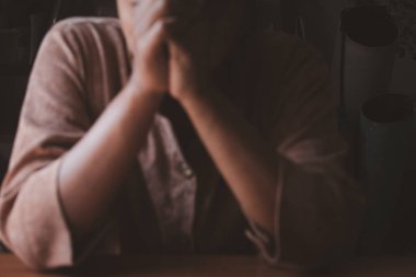 Blurred image of woman holding hands praying in vintage tones.For background.