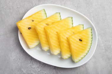 Beyaz tabakta sarı dilimlenmiş karpuz, yaz meyvesi.