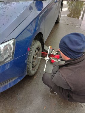 Suçlu görünümlü kimliği belirsiz bir adam özel bir anahtarla arabanın arka tekerleğini söker.