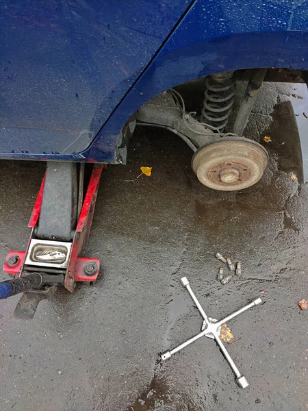 Changing a wheel on a car jack at a car service station on wet asphalt