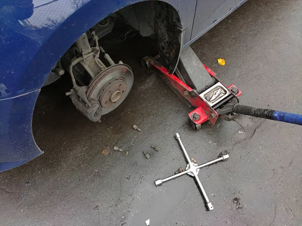 Changing a wheel on a car jack at a car service station on wet asphalt