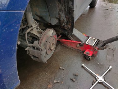 Islak asfalt üzerinde araba servis istasyonunda araba krikosunda tekerlek değiştirmek