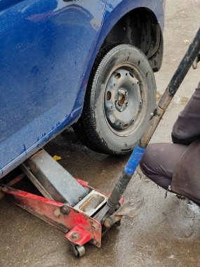 Islak asfalt üzerinde araba servis istasyonunda araba krikosunda tekerlek değiştirmek