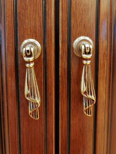 Two vintage identical hanging metal knobs on a wooden cabinet door close-up