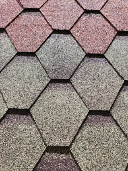 The roof is covered with hexagonal asphalt soft tiles close-up. Abstract geometric background on the theme of modern architecture or construction industry.