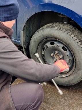 Otomobil tamircisi arabanın tekerleğinin yanına oturur ve vidaları yerine koymak için özel bir anahtarla söker.