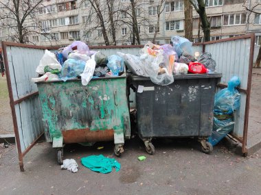 Two iron garbage containers full of various garbage on the street near a high-rise building