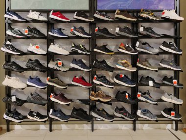 Rows of different sneakers of different brands are displayed on the shelves of a shoe store. Editorial photo on trade topics