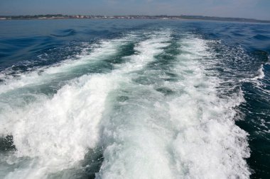 Texture of beautiful stormy waves in the ocean behind the ship. In the distance in the background is a city on the shore