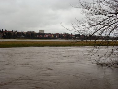 Spring flood. A wide river burst its banks and overflowed. A view of a small town across the river. Very gloomy weather