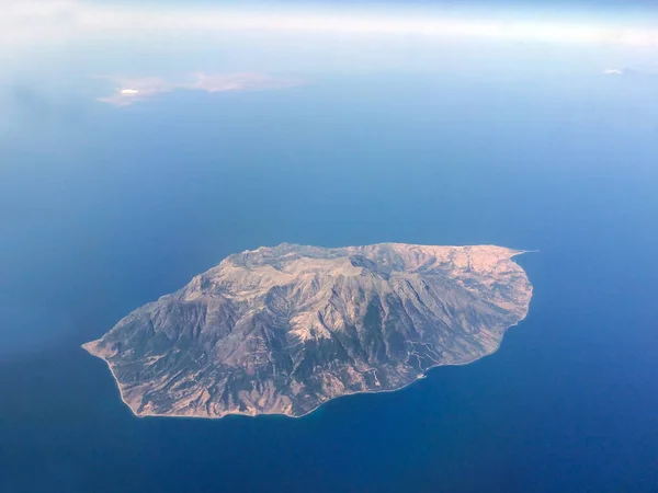 View from the plane of the majestic island below in the blue sea. There is another island in the distance