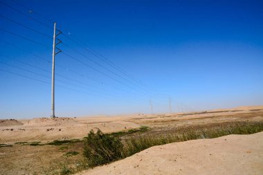 Yüksek voltajlı elektrik direkleri çölün perspektifinde mavi gökyüzünün arka planına karşı.