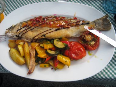 Limonlu, domatesli, patatesli kızarmış balık, yakın plandaki bir tabakta. En üstten, bıçak tarafından.