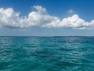 Deniz ve gökyüzü çeşitli türkuaz ve mavi tonlarda. Beyaz bulutlu parlak doğal arkaplan